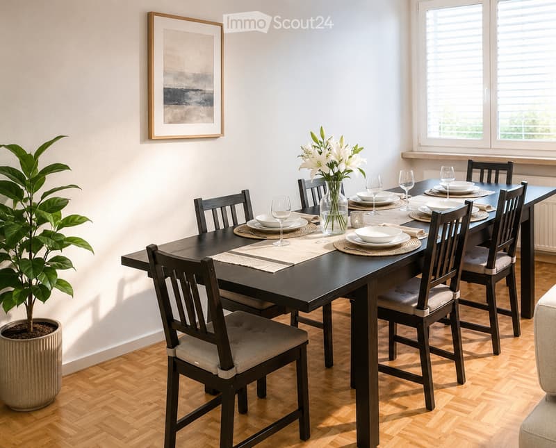 Dining room with a dark wooden table set for six, surrounded by six chairs with beige cushions. A vase with white lilies is placed at the center of the table, and wine glasses are set around. A potted plant is on the left side, and a framed picture hangs