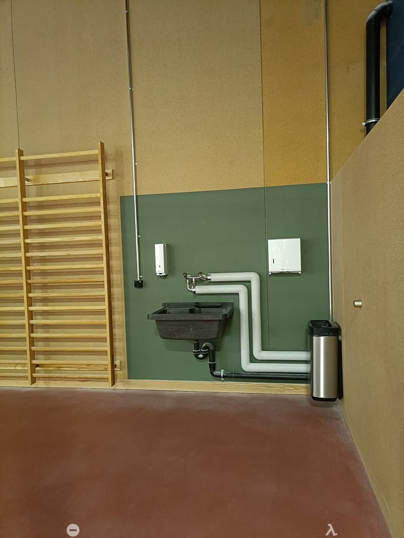 Bathroom with a black sink, faucet, soap dispenser, paper towel dispenser, and a trash can. Wooden shelf on the left side.