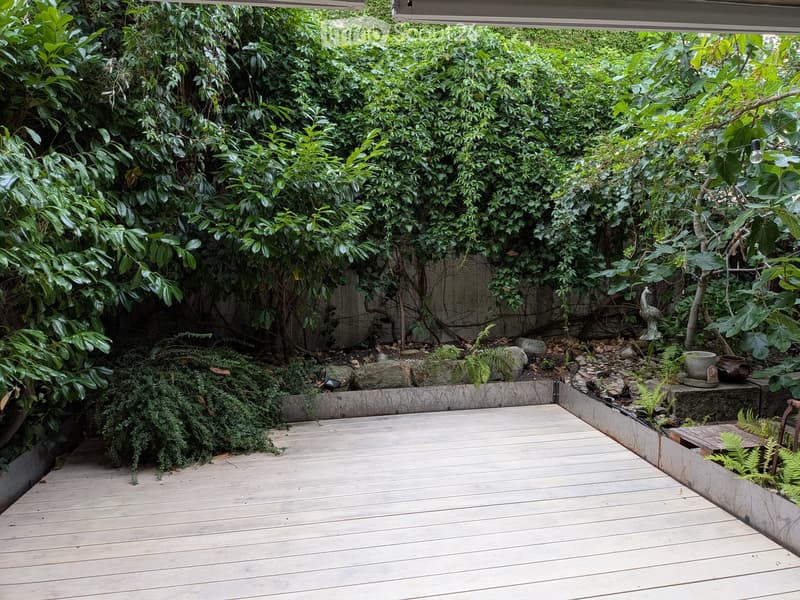 Wooden deck surrounded by lush greenery, with small garden beds and decorative elements.