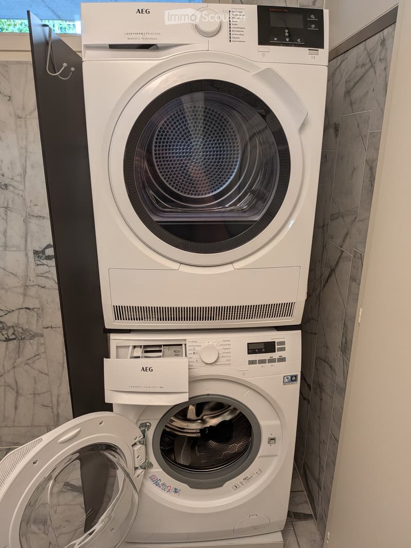 A modern bathroom with a white AEG washing machine and dryer stacked vertically, featuring digital control panels and sleek design.