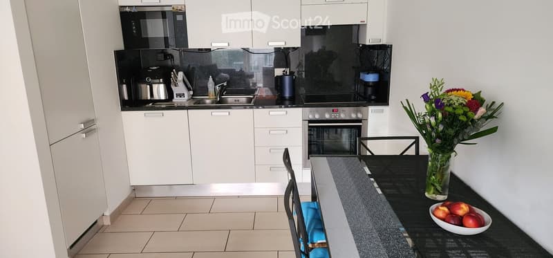 Modern kitchen with white cabinets, stainless steel appliances, and a black countertop. Includes a microwave, coffee maker, oven, sink, and a dining area with a table, chairs, and a vase of flowers.