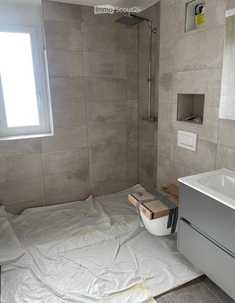 Bathroom with tiled walls, a shower area, a sink, and a toilet covered in protective plastic sheeting.