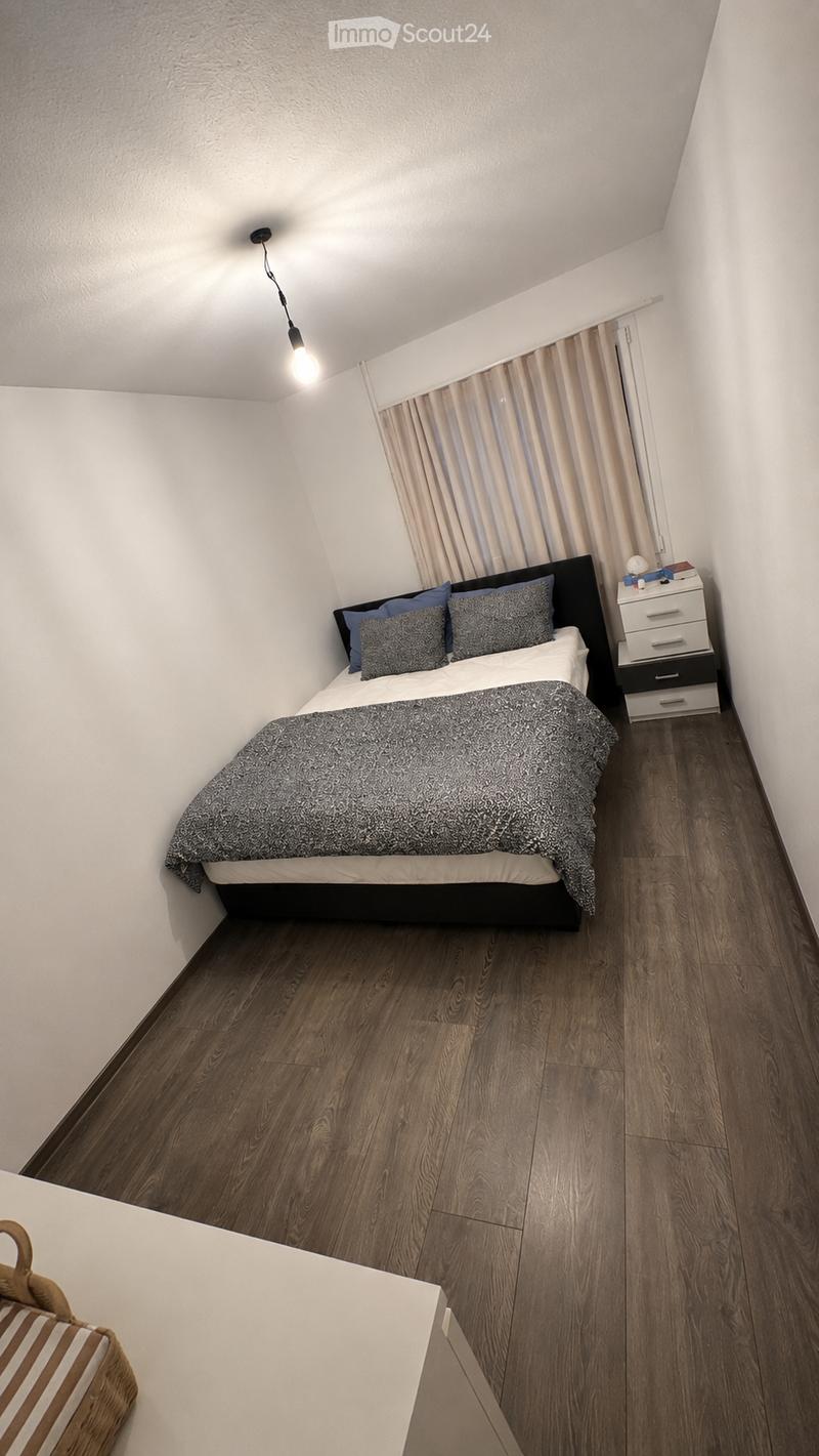 Cozy bedroom with a double bed, nightstand, and a hanging lamp. The room features wooden flooring and white walls.