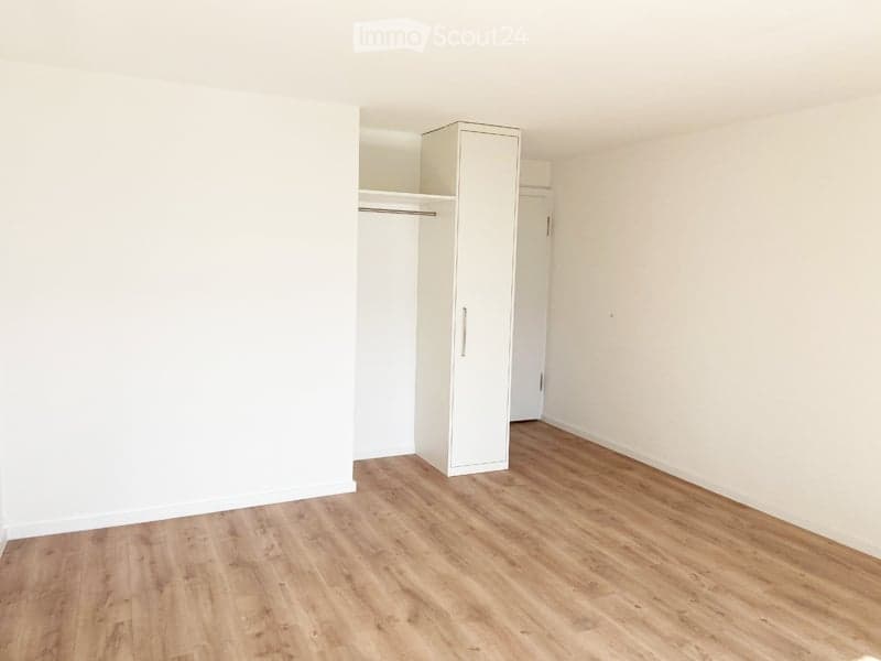 Empty room with light wooden flooring and white walls, featuring a built-in closet with a sliding door.