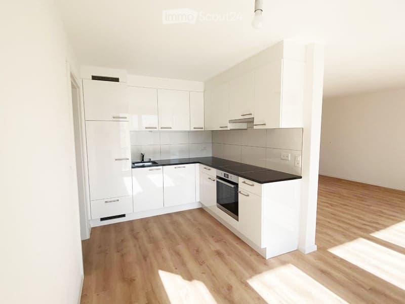 Modern kitchen with white cabinets, black countertops, and wooden flooring. Features include a sink, oven, and faucet.