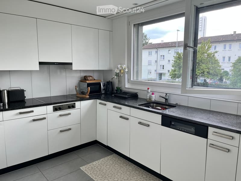 Modern kitchen with white cabinets, black countertops, and stainless steel appliances. Features a sink, oven, microwave, toaster, and dishwasher.
