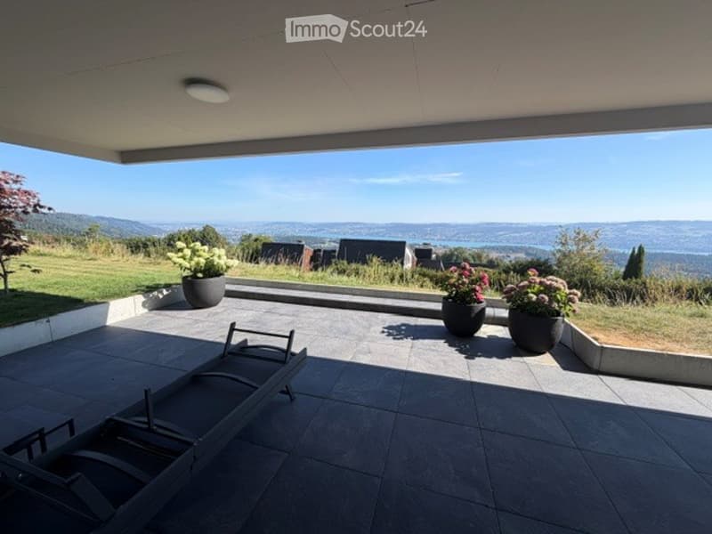 Modern balcony with expansive scenic view, tiled floor, lounge chairs, and potted plants.