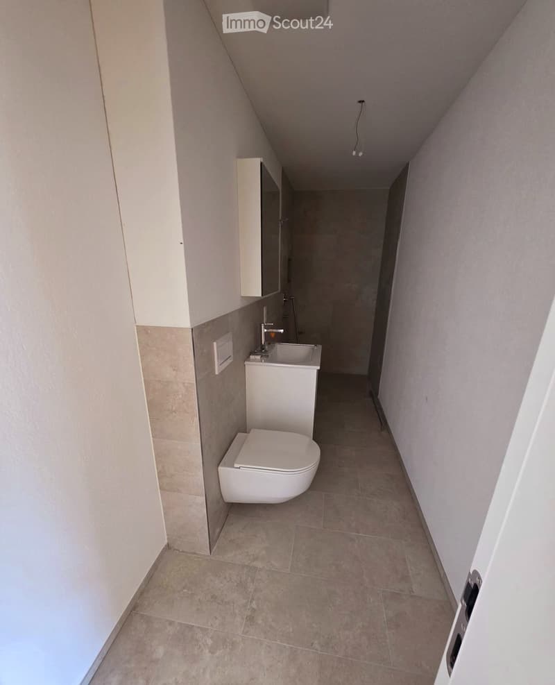 Modern bathroom with a toilet, sink, and cabinet, featuring beige tiled walls and floor.