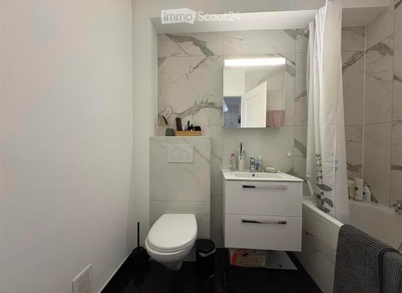 Modern bathroom with white marble tiles, a white toilet, a white sink with a mirror above it, and a shower area with a curtain.