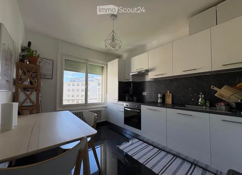 Modern kitchen with white cabinets, a dining table with chairs, a window with a view, and various appliances including an oven and sink.