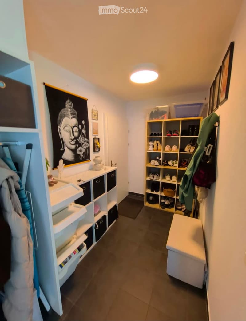 Well-lit hallway with white walls, dark tiled floor, built-in storage units, and a bench at the end.