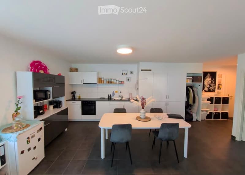 Modern kitchen and dining area with white cabinets, black appliances, a dining table with four chairs, and decorative items on shelves and counters.