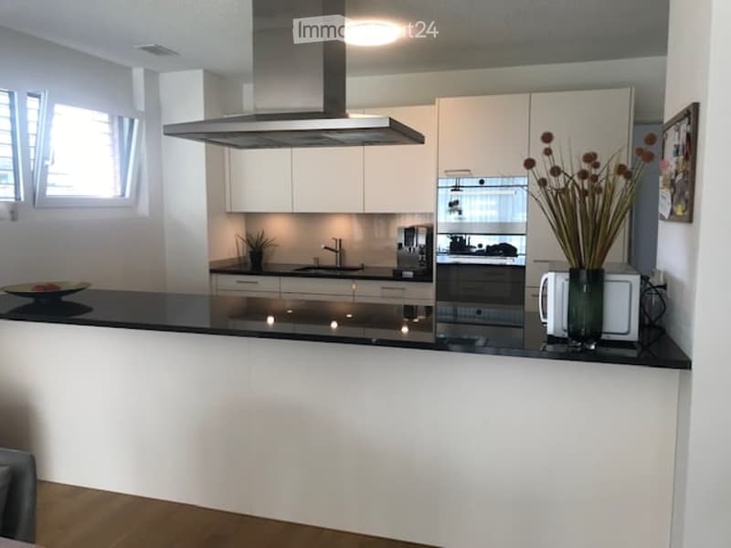 Modern kitchen with white cabinets, stainless steel appliances, and a black countertop. Features include a faucet, oven, microwave, and decorative vase with flowers.
