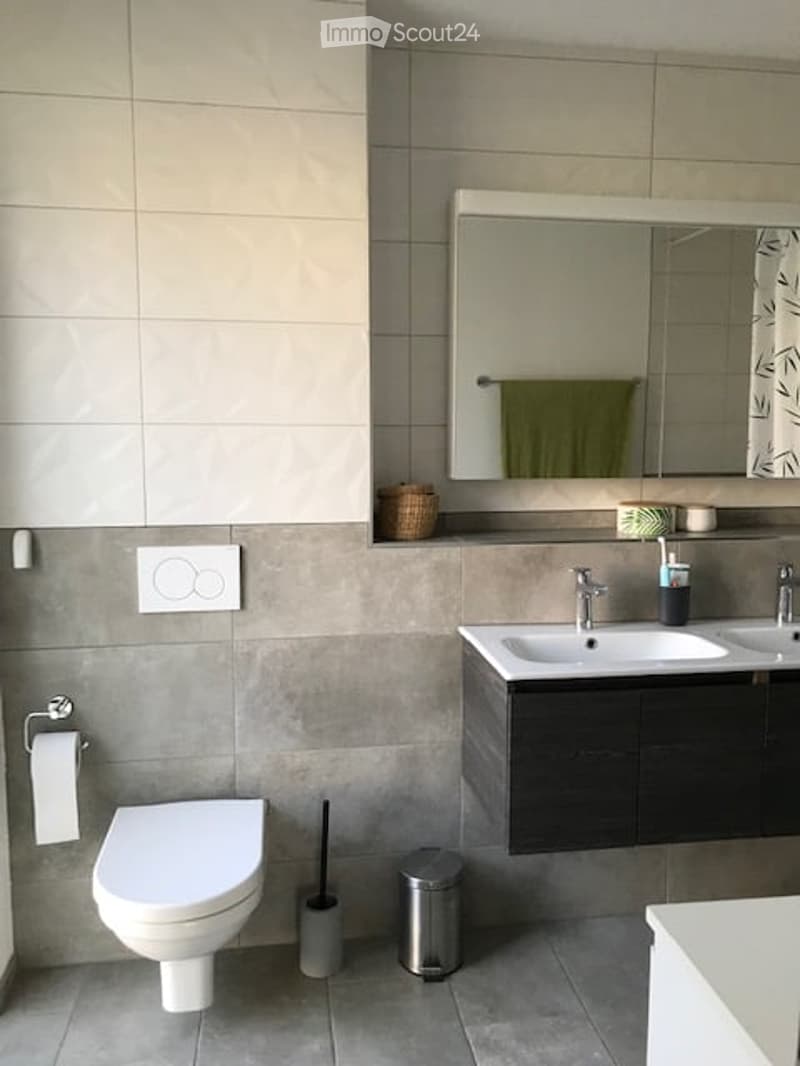 Modern bathroom with a white toilet, double sink vanity, large mirror, and tiled walls.