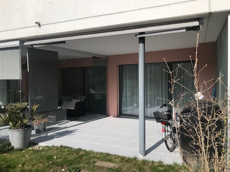 Modern outdoor patio with large retractable glass doors leading to a living space, potted plants, and a bicycle parked nearby.