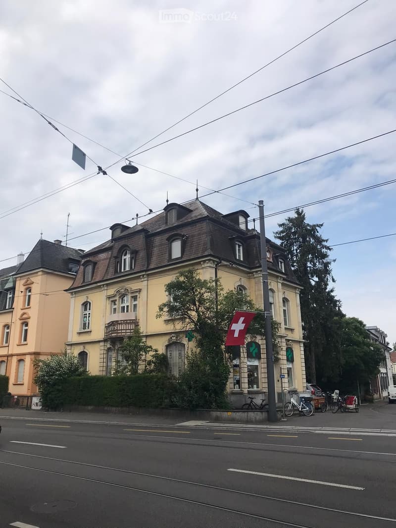 A multi-story building with a classic facade, featuring arched windows, a balcony, and a Swiss flag displayed on a pole.