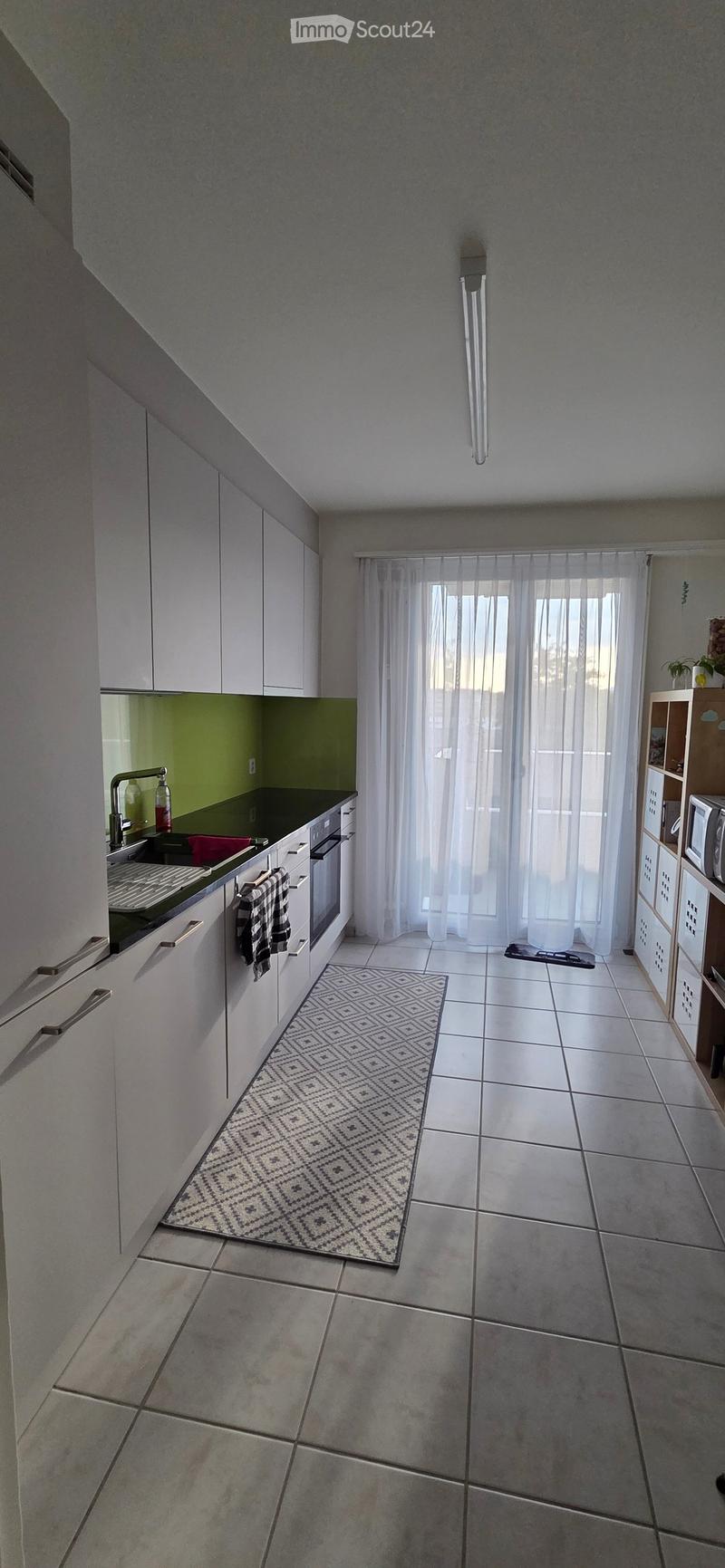 Modern kitchen with white cabinets, a black countertop, a sink with a faucet, an oven, a microwave, and a patterned rug on the floor.