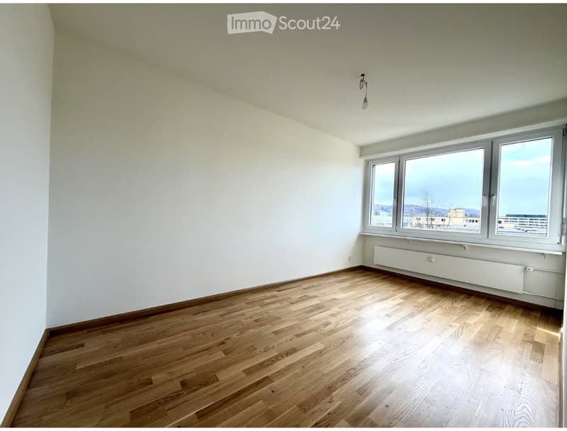 Empty room with wooden flooring, white walls, large windows, and a radiator. No furniture or equipment present.
