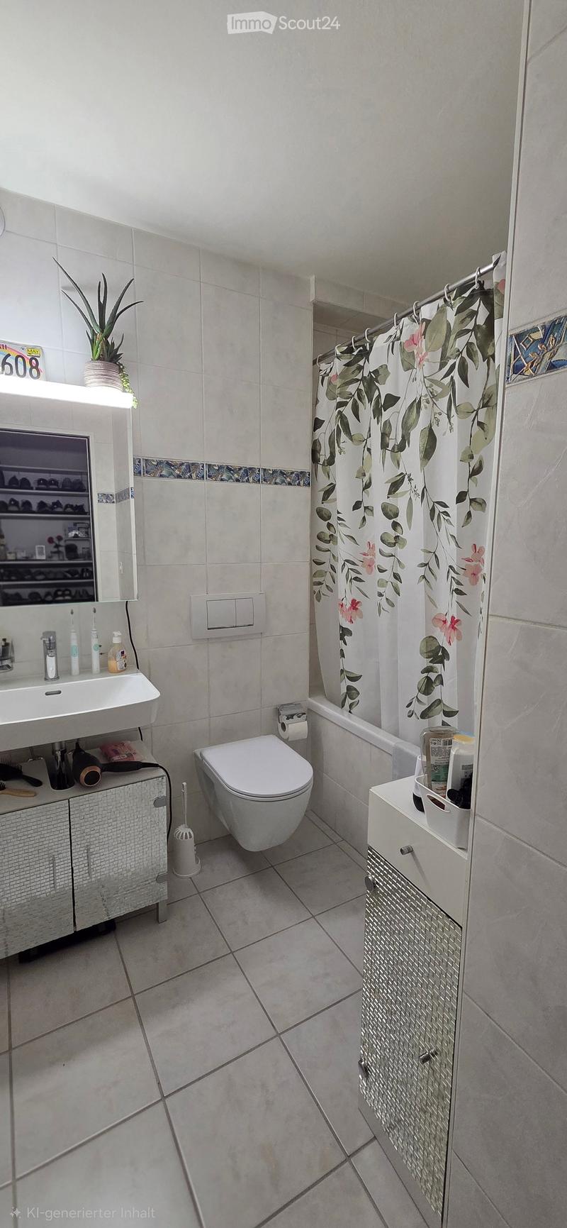 Modern bathroom with white tiles, a sink, toilet, mirror, and a shower area with a floral curtain. Includes a small cabinet, plant, and various toiletries.