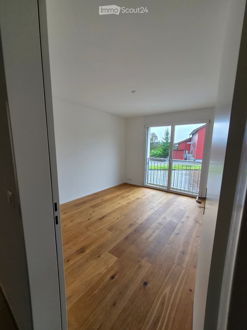Empty room with light wooden flooring and white walls, featuring a large sliding glass door leading to an outdoor area.