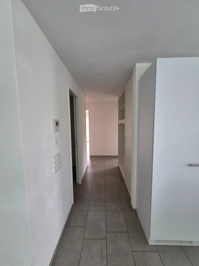 Empty hallway with white walls, tiled floor, and built-in shelving unit on one side.