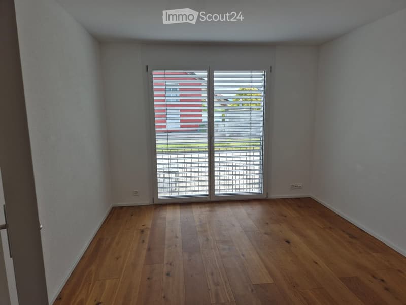 Empty room with wooden flooring, white walls, and large sliding glass door with blinds.