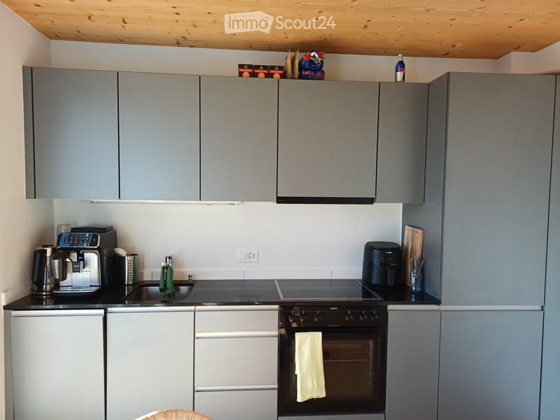 Modern kitchen with grey cabinets, stainless steel appliances, and a black countertop. Features a coffee maker, oven, fridge, sink, and various kitchen utensils.