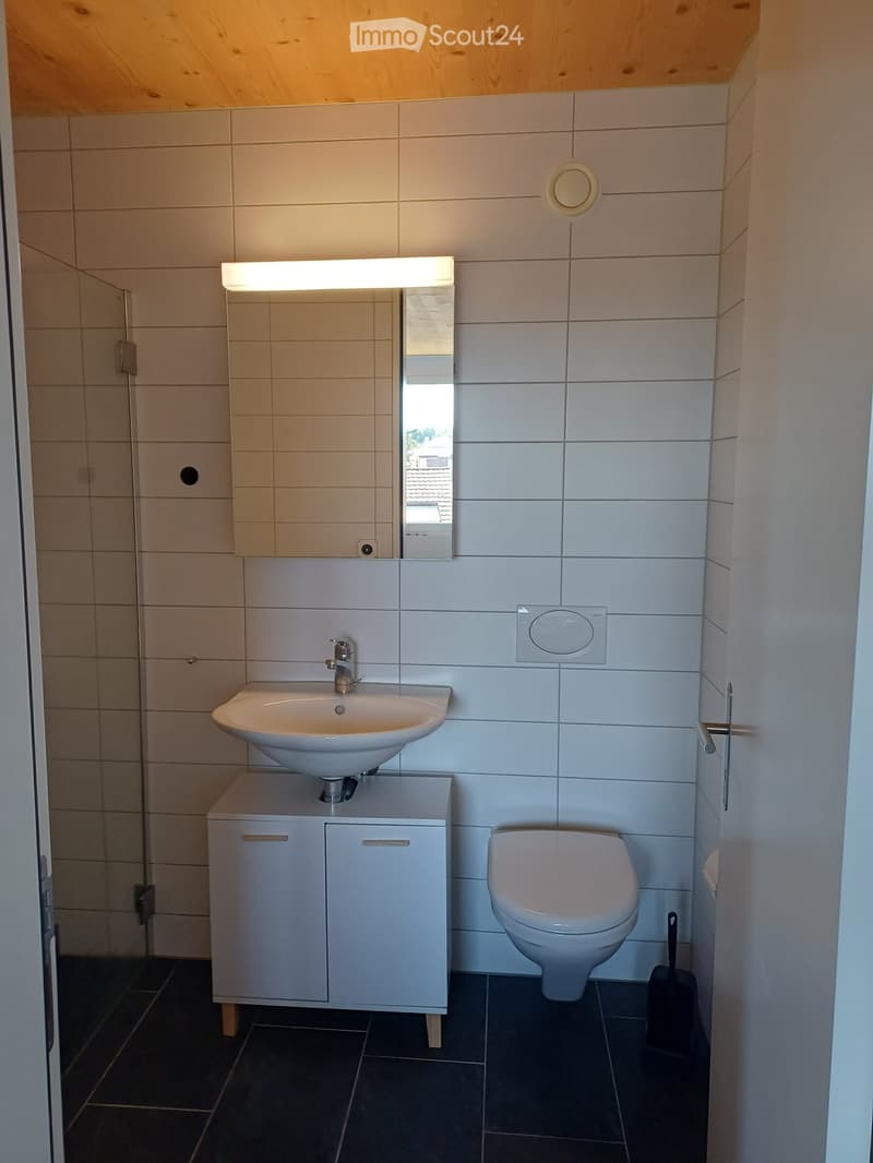 Modern bathroom with white tiles, a sink with a cabinet, a toilet, a mirror with built-in lighting, and a dark tiled floor.