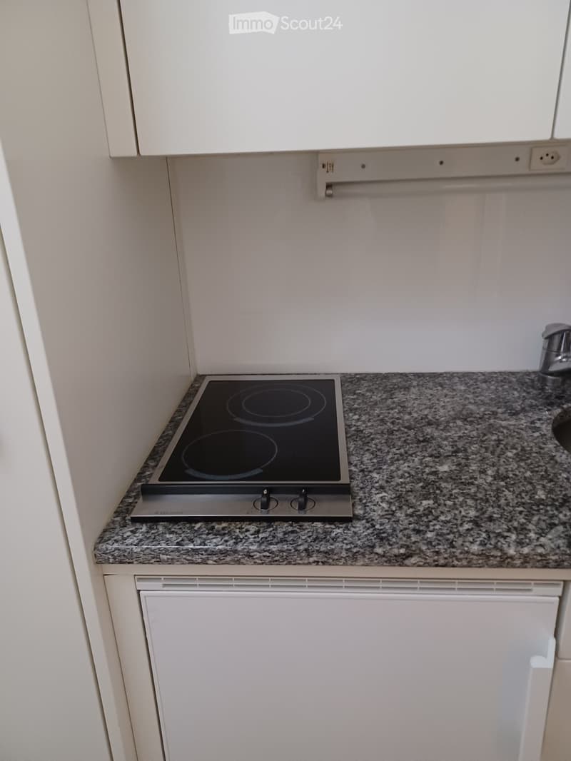 Modern kitchen with granite countertop, induction stove, and white cabinets.