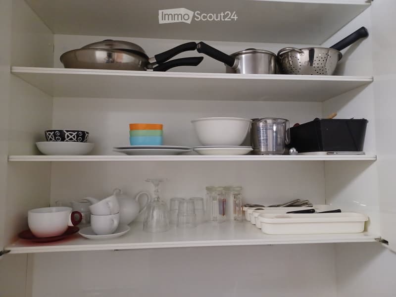 Open kitchen cabinet with neatly arranged kitchenware including pots, pans, bowls, cups, and glassware on multiple shelves.