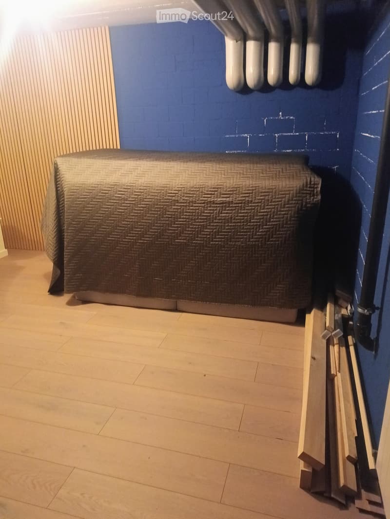 Bedroom with a single bed covered in a patterned duvet, light wooden flooring, and blue accent wall.