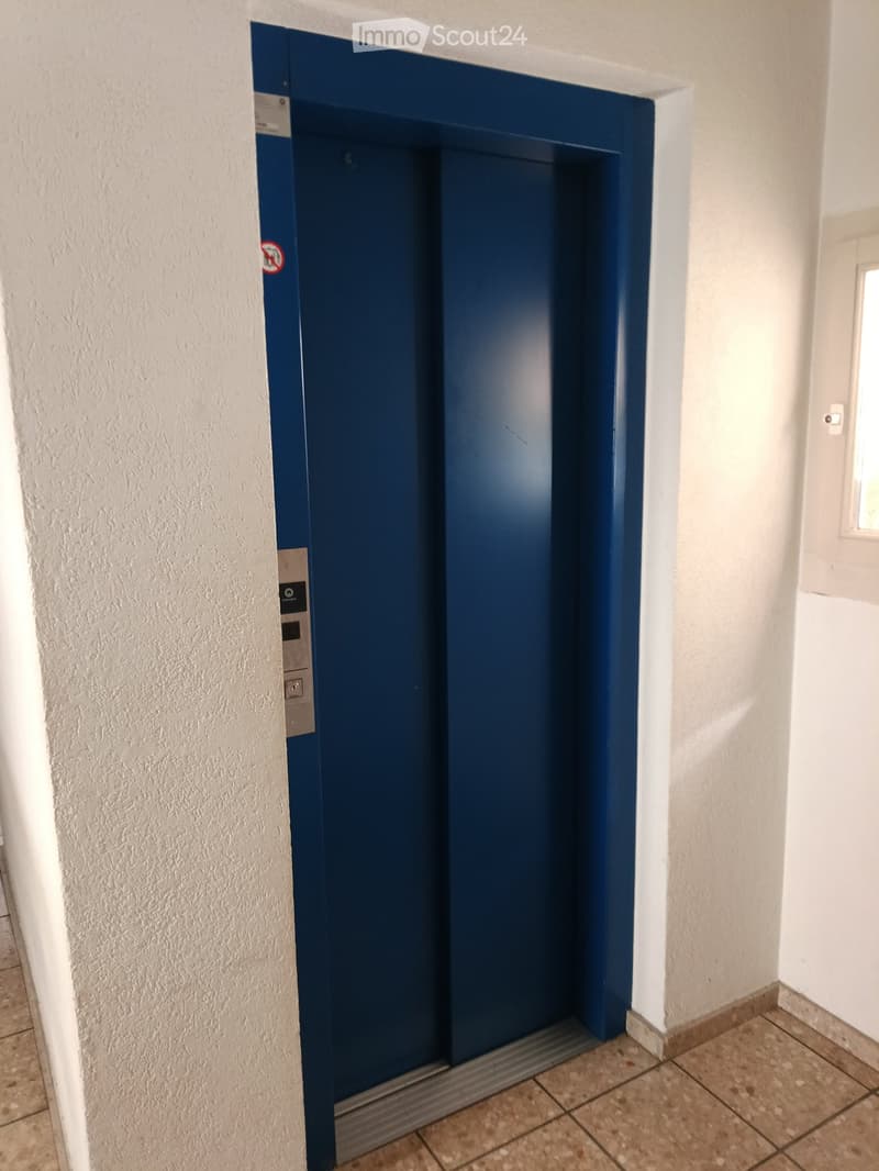 A hallway with a closed elevator door, white walls, and tiled floor.