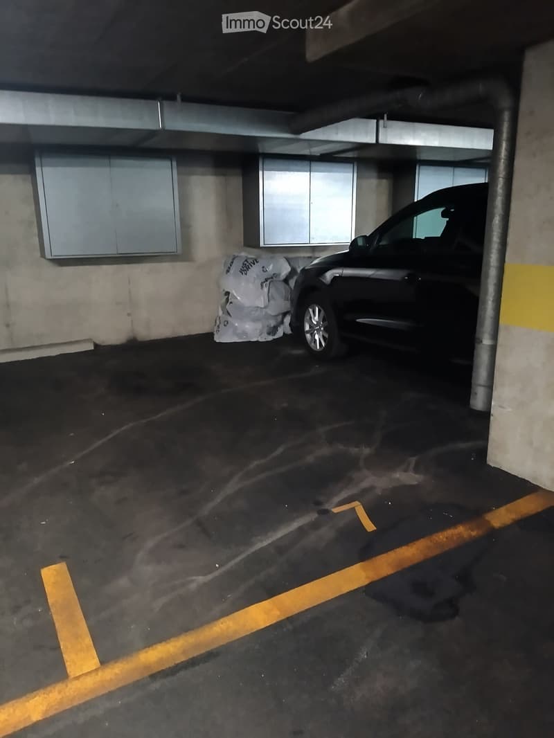 Underground parking area with a parked car and some plastic bags on the floor.