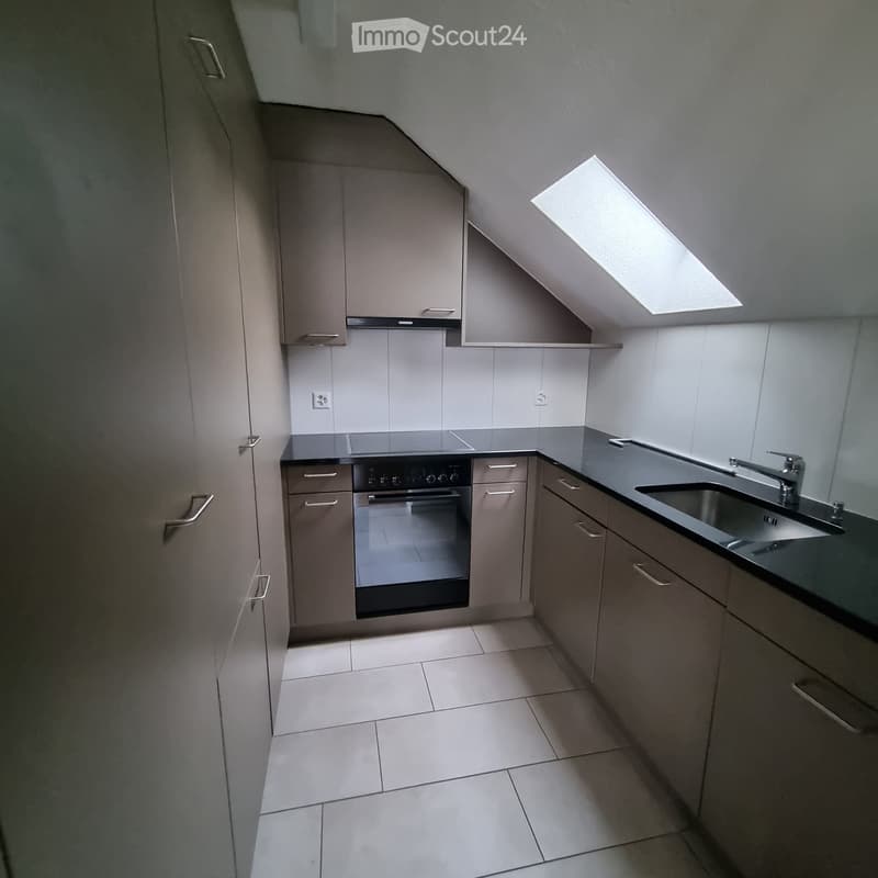 Modern kitchen with grey cabinets, a stainless steel sink, and an oven. The space features a skylight and tiled flooring.