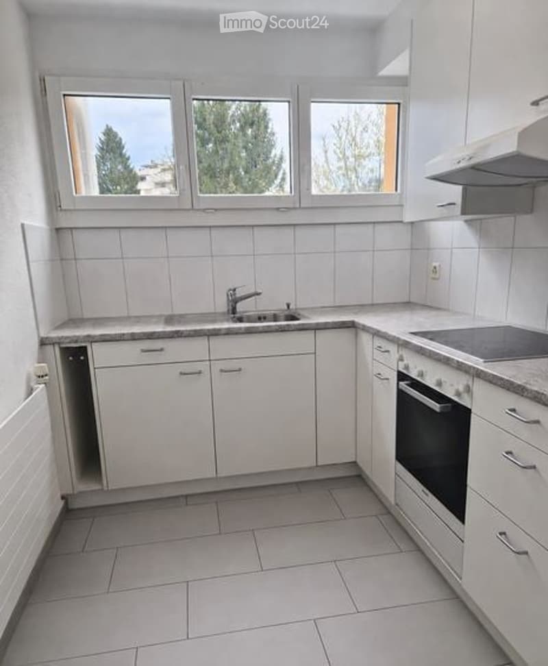 Modern kitchen with white cabinets, tiled walls, and a countertop with a sink and oven.