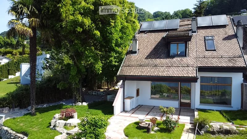 Modern two-story house with solar panels on the roof, large windows, and a well-maintained garden with a stone pathway and various plants.