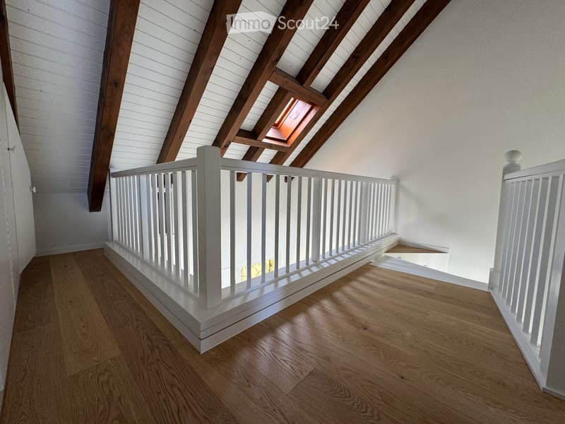 Spacious hallway with wooden flooring, white painted wooden railing, exposed wooden beams, and a skylight window at the top.