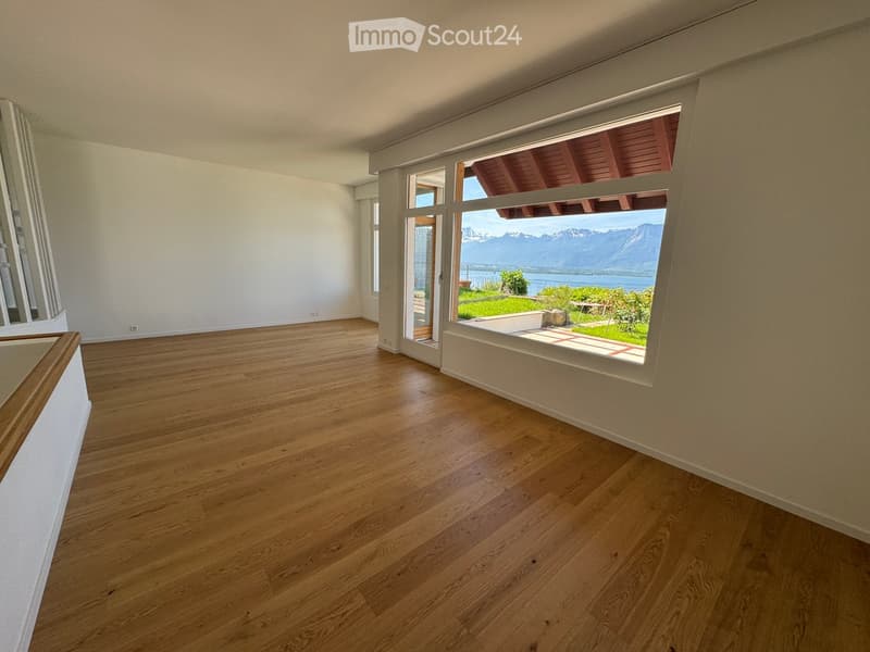 Empty room with wooden flooring, large windows offering a scenic mountain and lake view, and a sliding glass door leading to an outdoor patio.