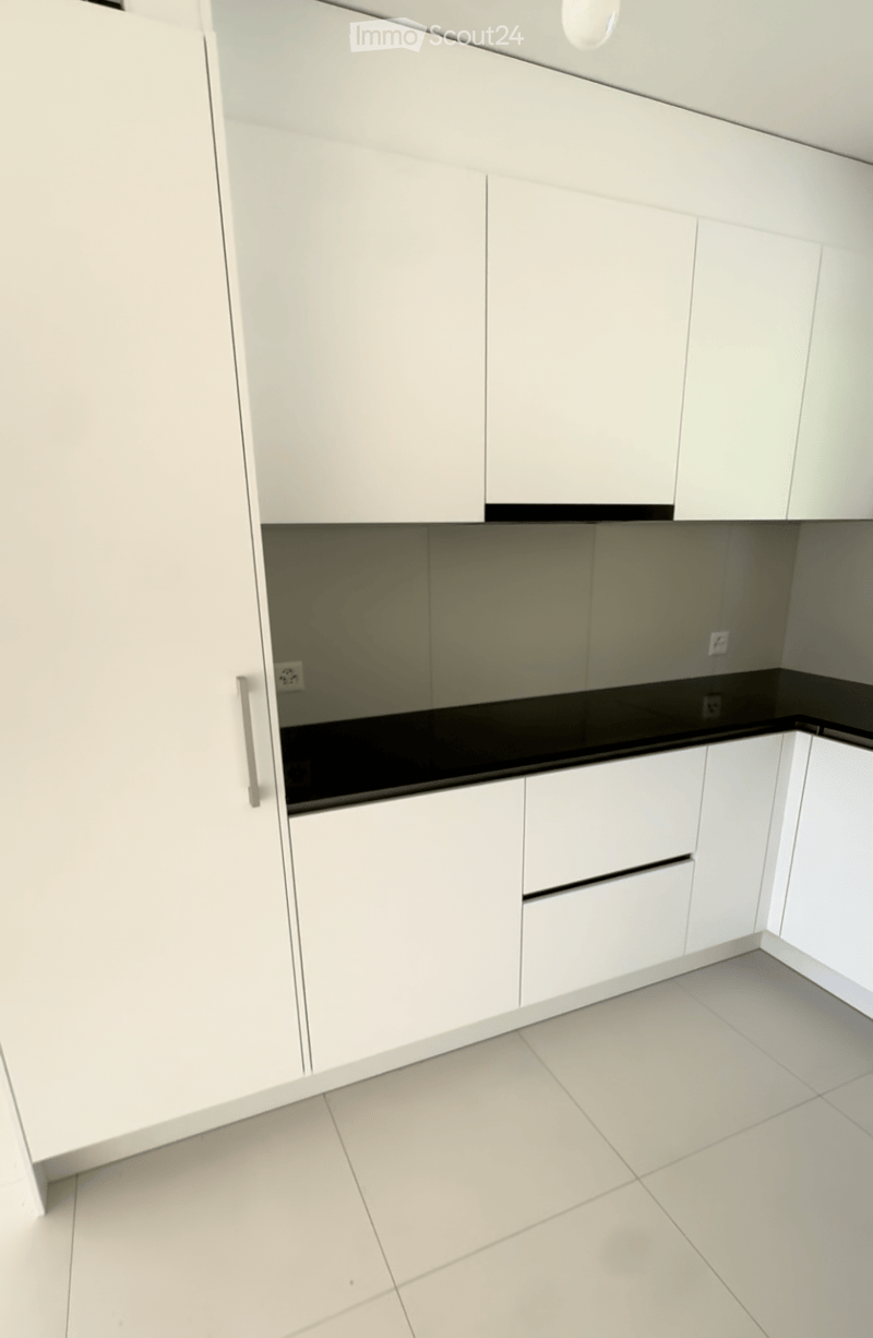 Modern kitchen with white cabinets, black countertop, and tiled floor.