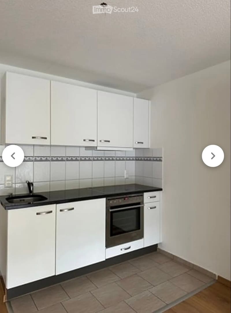 Modern kitchen with white cabinets, black countertop, sink, and built-in oven. Tile backsplash and tiled floor.