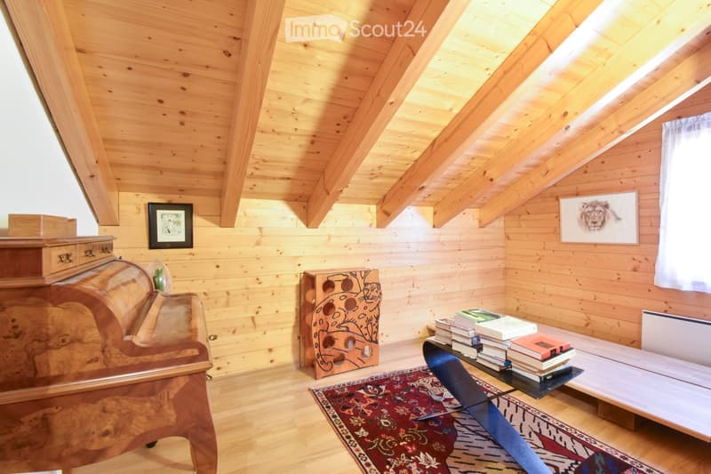 Cozy attic room with wooden walls and ceiling, featuring a sofa, a small table with books, a framed picture, and a decorative cabinet.