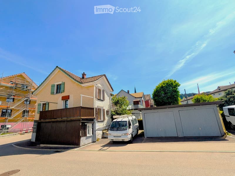 Two-story house with beige and white exterior, green shutters, balcony, garage, and driveway with a parked van.