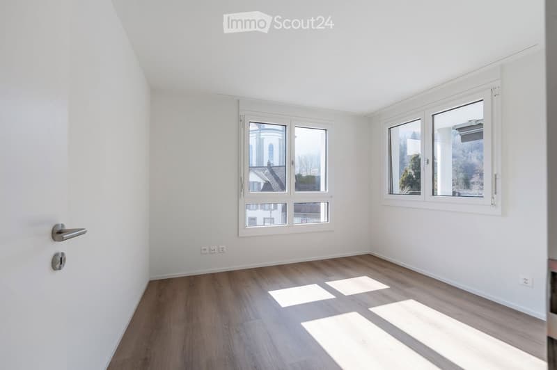 Empty room with white walls, wooden floor, and two large windows. No furniture or equipment.