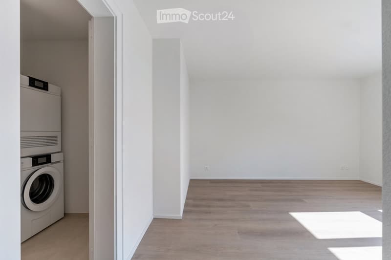 An empty room with white walls, wooden floor, and a built-in washer and dryer.