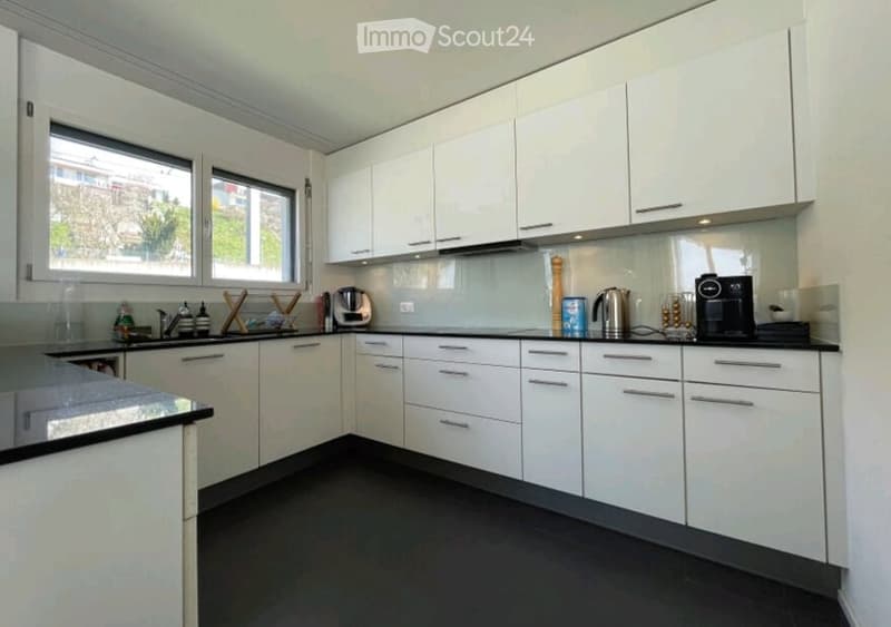 Modern kitchen with white cabinets, black countertops, and stainless steel appliances. Features include a sink, coffee maker, and various kitchen items on the counter.