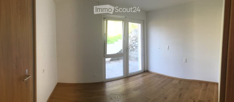 Empty room with wooden flooring, white walls, and a large sliding glass door leading outside.