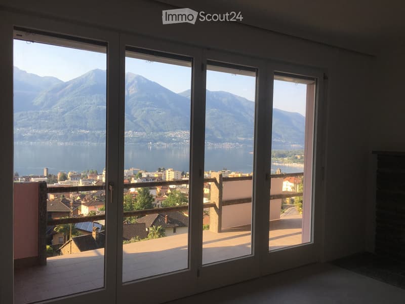 Large balcony with expansive view of a lake and surrounding mountains, accessible through large glass doors.