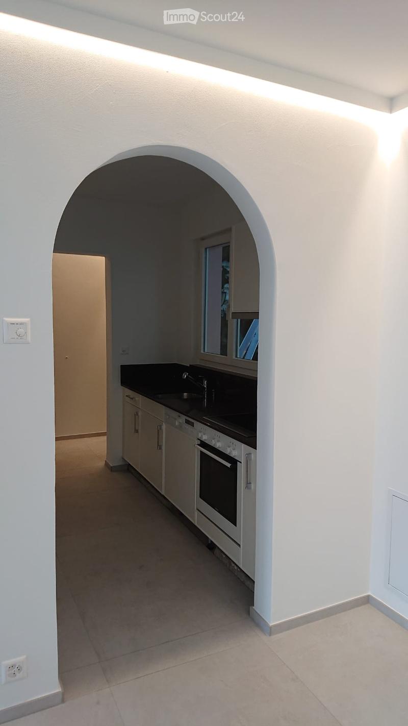 Modern kitchen with white cabinets, black countertop, sink, faucet, and built-in oven. Features an arched entryway and tiled flooring.