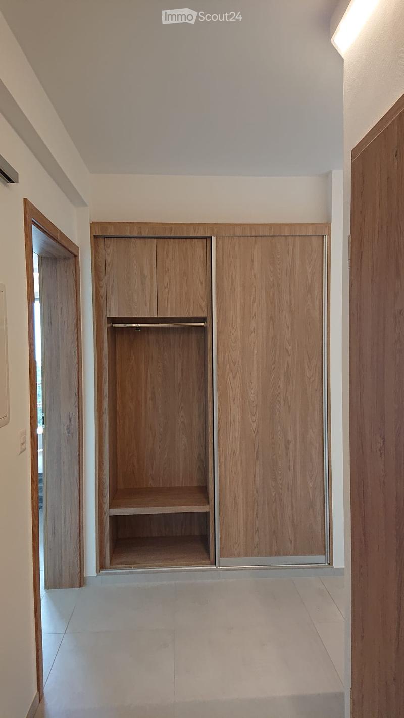 Empty hallway with light-colored walls, tiled floor, and a built-in wooden closet with open shelving and closed cabinet doors.