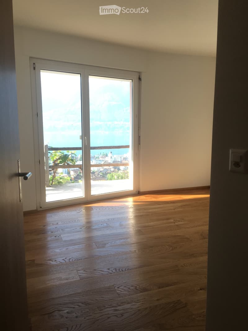 Empty room with wooden flooring and large sliding glass doors leading to a balcony with a scenic view.